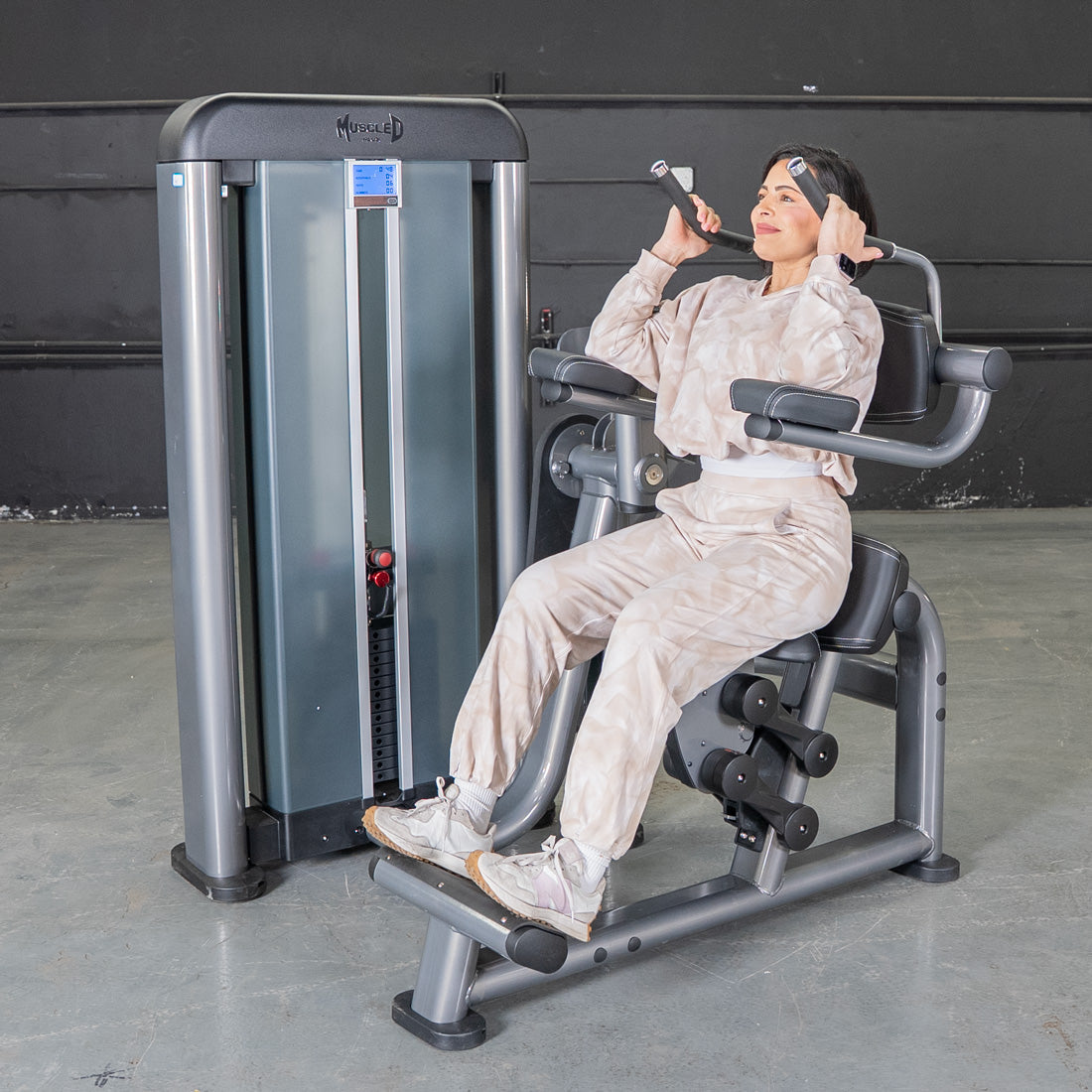 Woman using MuzzleD gym machine in neutral tracksuit for core workout.