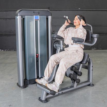 Woman using MuzzleD gym machine in neutral tracksuit for core workout.