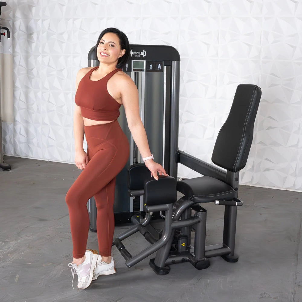Fit woman in rust activewear standing beside an outer thigh machine in gym.