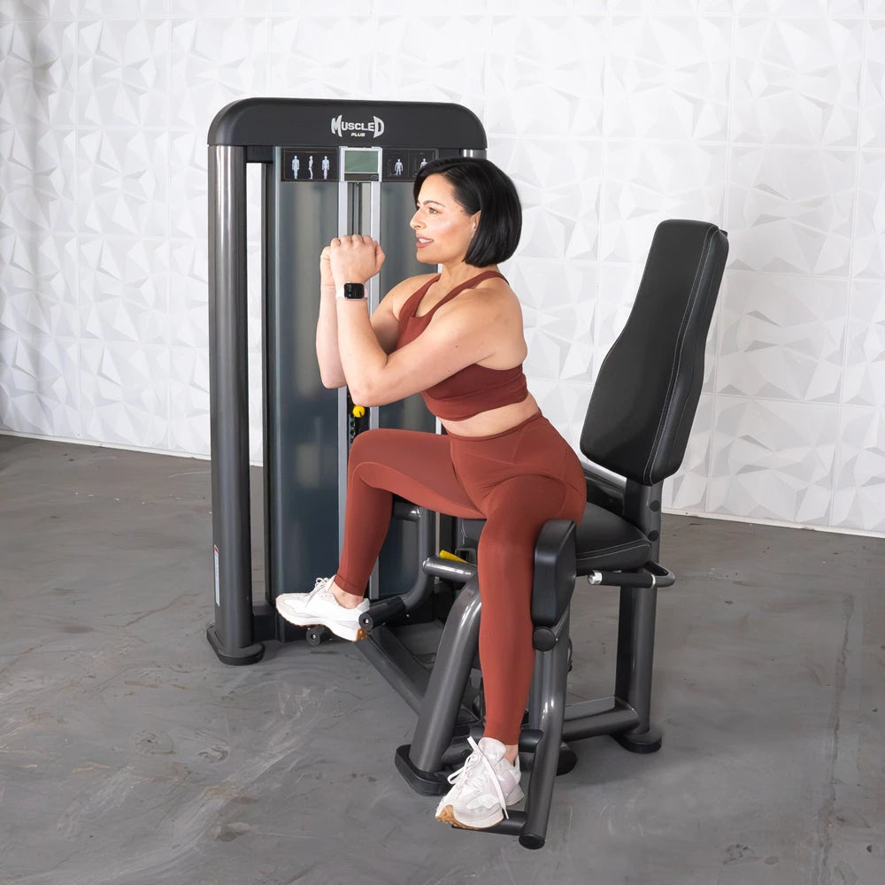 Woman in rust activewear uses an outer thigh machine at the gym.