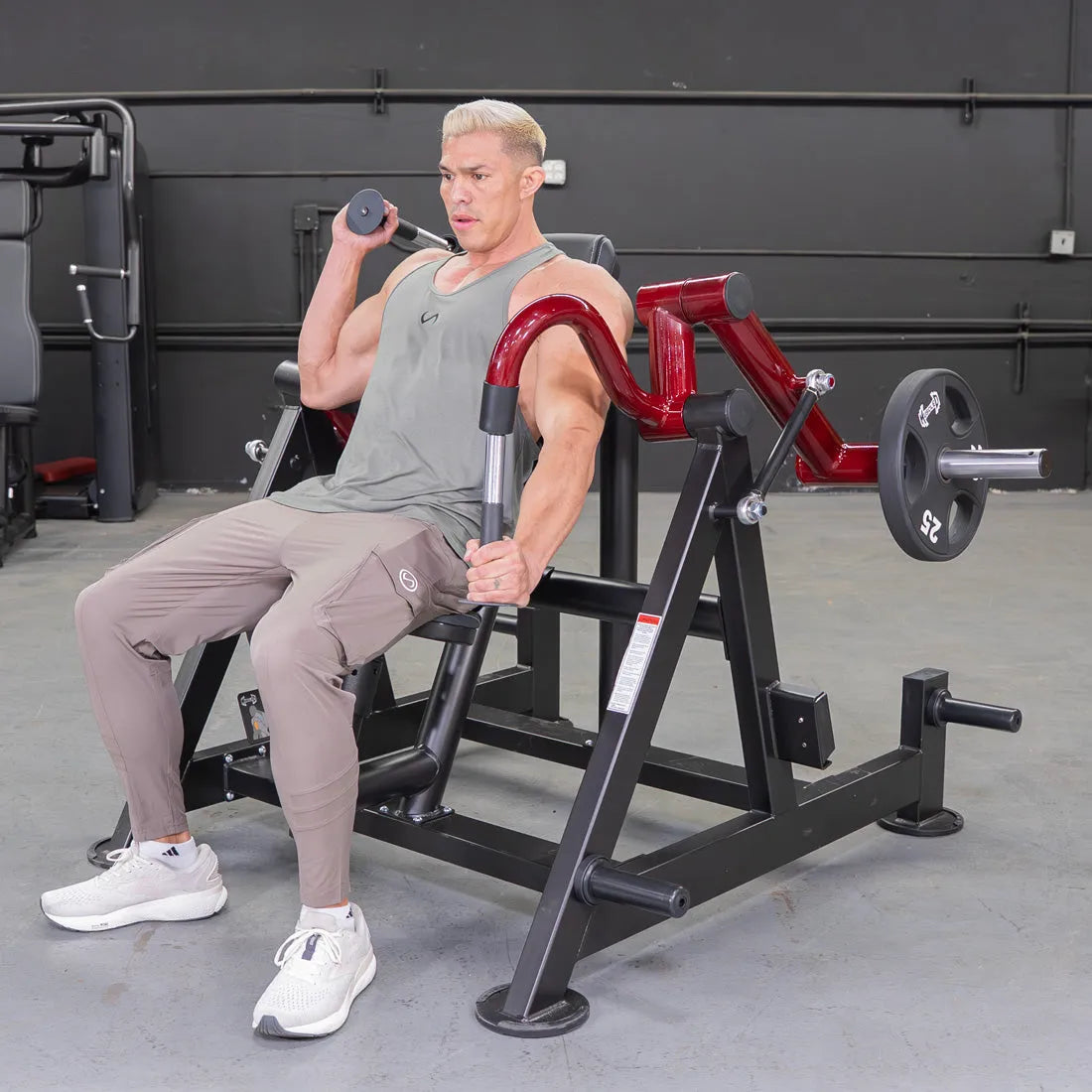 Man seated on leverage triceps machine with red arms in gym.