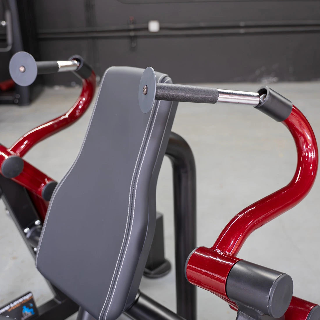 Hammer-grip triceps machine with red frame and gray padded seat.