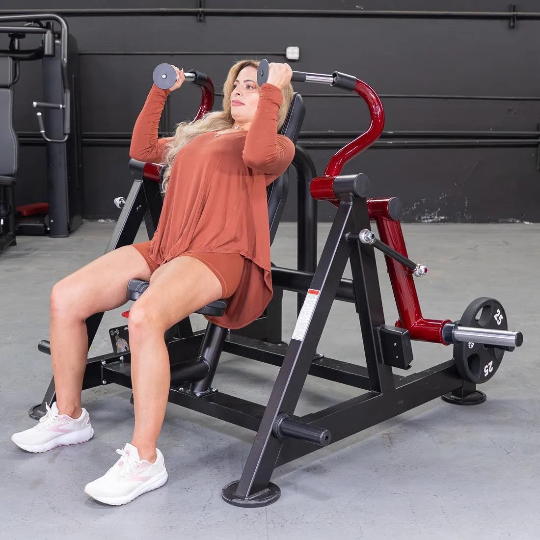 Woman performing triceps extension on hammer-grip machine in gym.