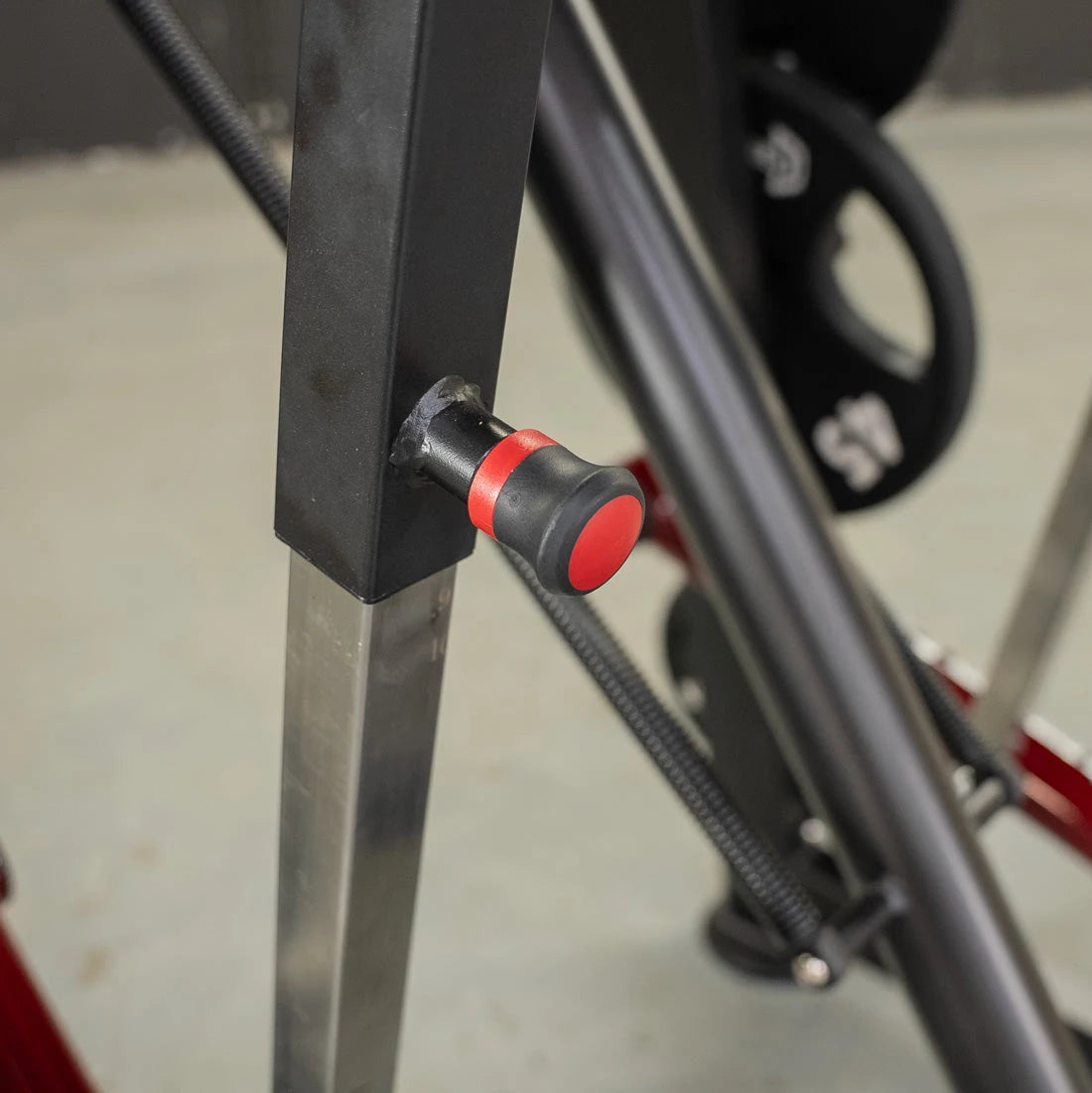 Red-topped adjustment knob on a black gym machine frame.