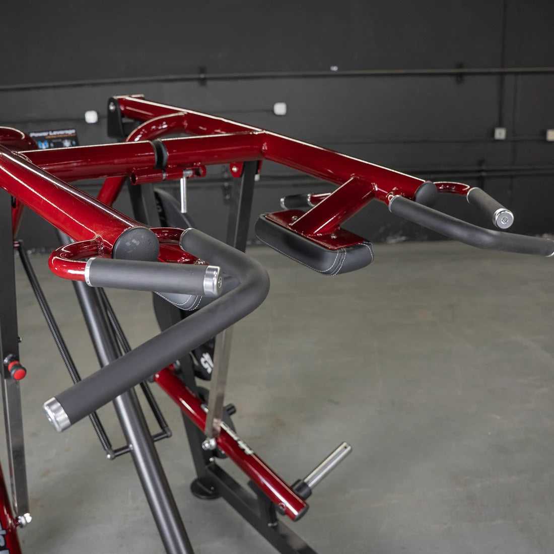 Red power-leverage gym machine with padded grips and calf press attachments.