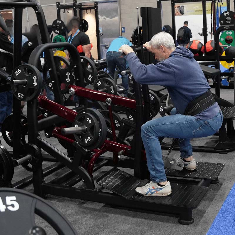 Man using a belt squat machine in a gym with weights and plates.