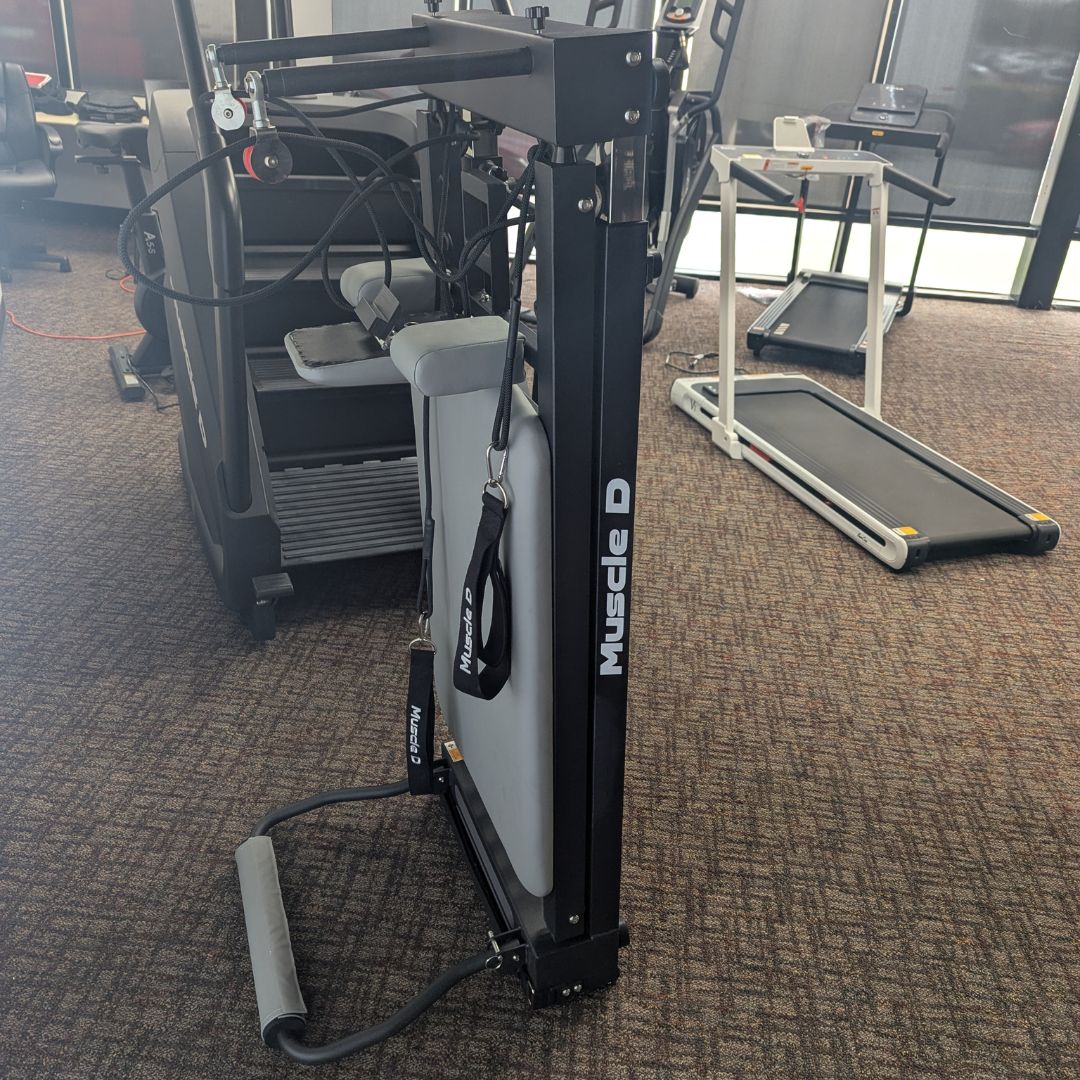Gym weight machine with padded seat and pulley arms, labeled Muscled.
