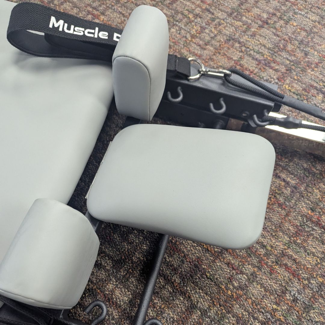 Gray padded cushions and straps for a Pilates machine leg support.