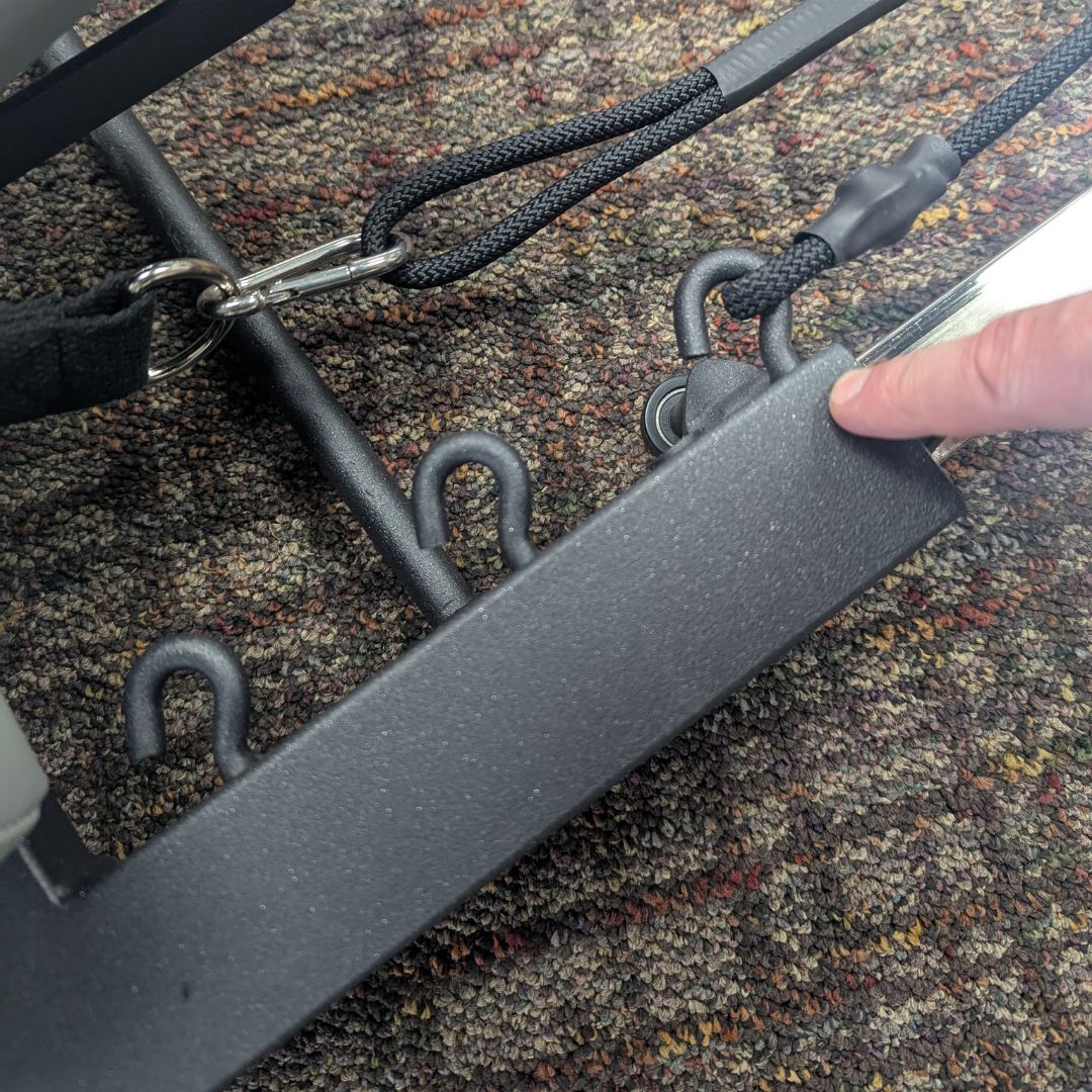 Close-up of a Pilates table frame with metal hooks and black straps.