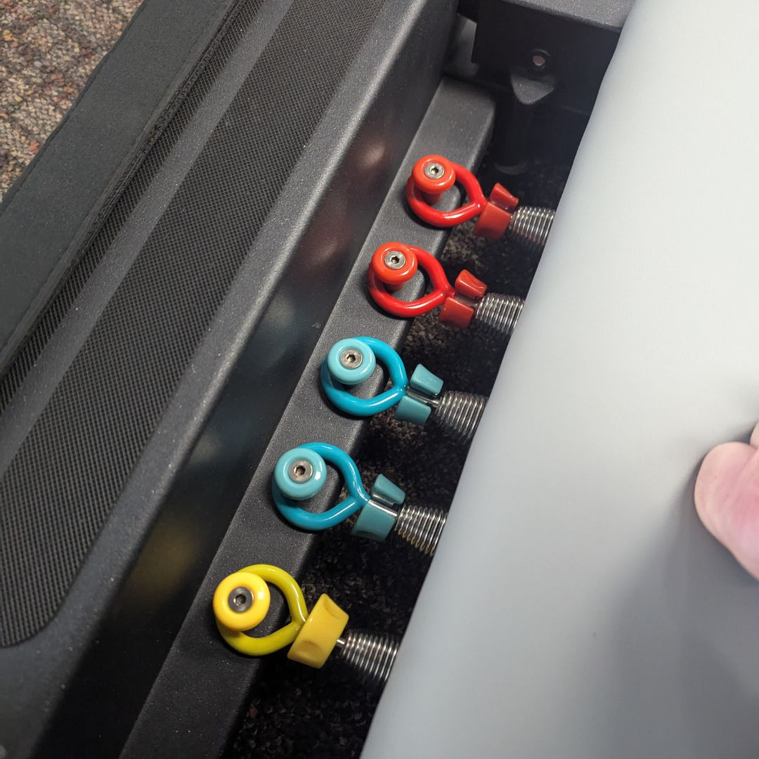 Row of colorful eye bolts with metal studs along equipment edge.
