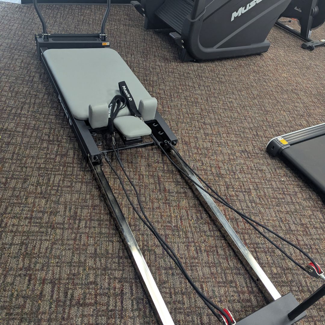 Pilates reformer machine with gray padded carriage and resistance straps.
