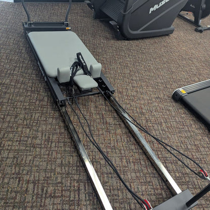 Pilates reformer machine with gray padded carriage and resistance straps.