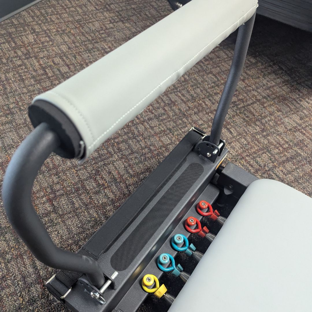Grey padded handbar with color-coded adjustment pins on a Pilates machine.