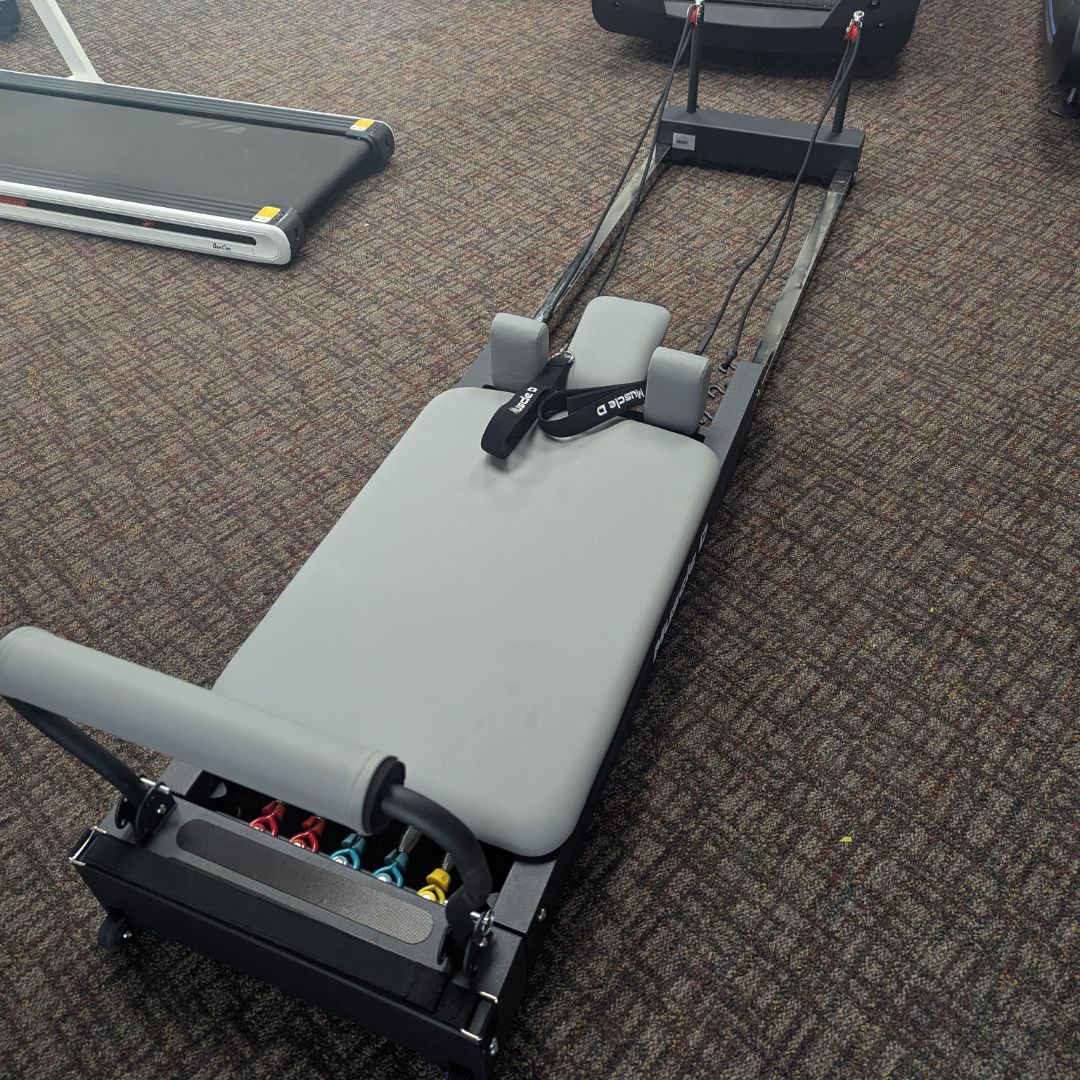 Pilates reformer with padded bench and colorful resistance springs on carpet.