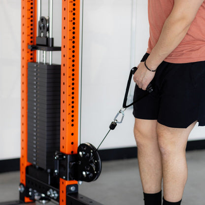 Person in pink shirt and black shorts using a cable machine by an orange rack.