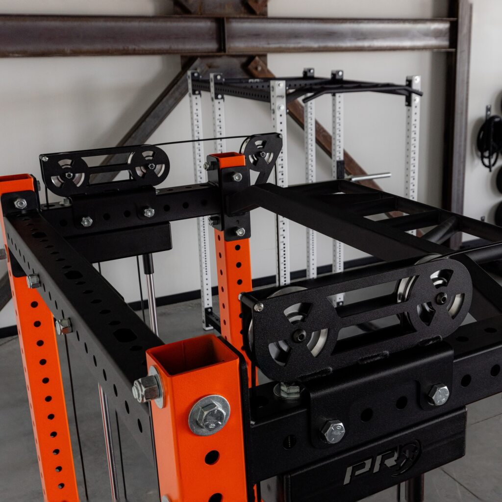 Industrial gym equipment: black steel frame with orange support posts and pulleys.