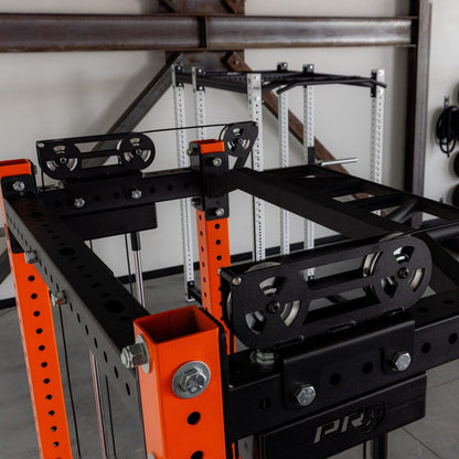 Industrial gym equipment: black steel frame with orange support posts and pulleys.