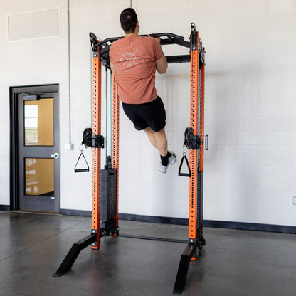 Man doing a pull-up on an orange power rack in a gym.