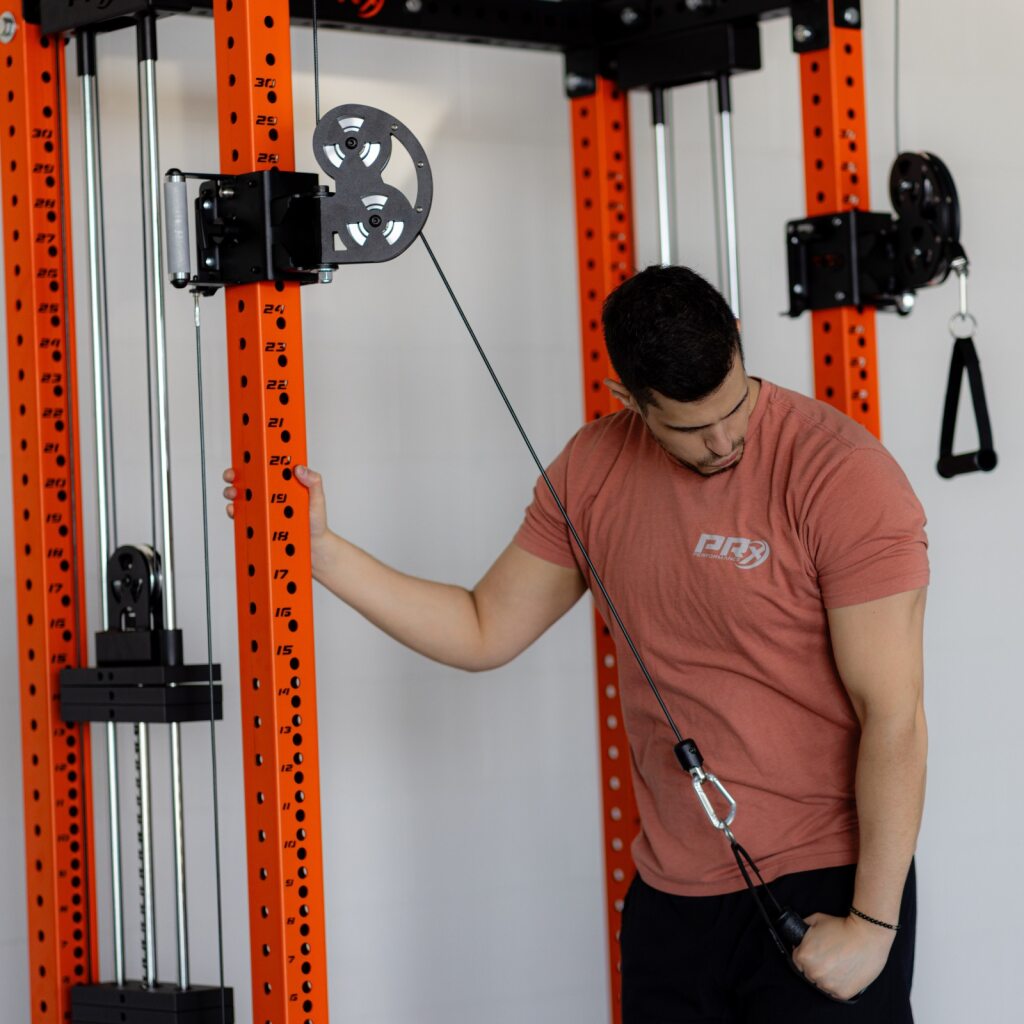 Man in pink t-shirt using a cable machine in a gym.