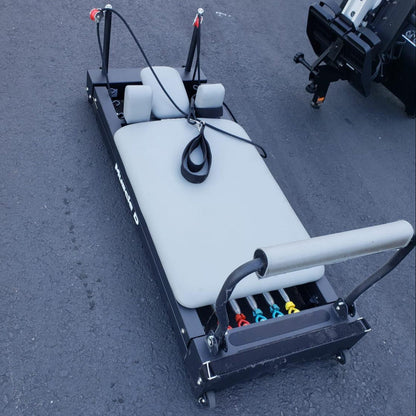 Pilates reformer with padded bench, straps, and color-coded springs.