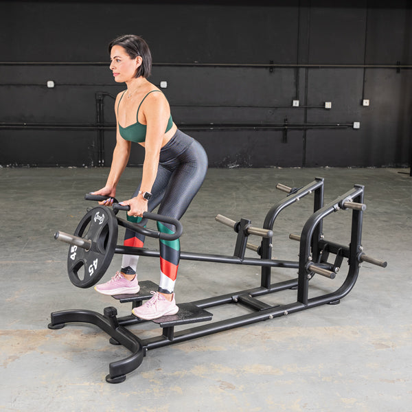 Woman using T-Bar Row Machine in gym, wearing colorful leggings and pink sneakers, focused on strength training.