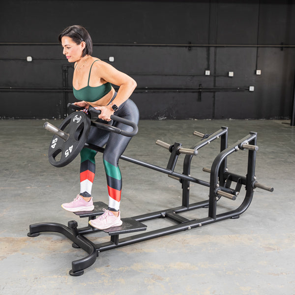 Woman using a T-Bar Row Machine with colorful leggings for strength training.
