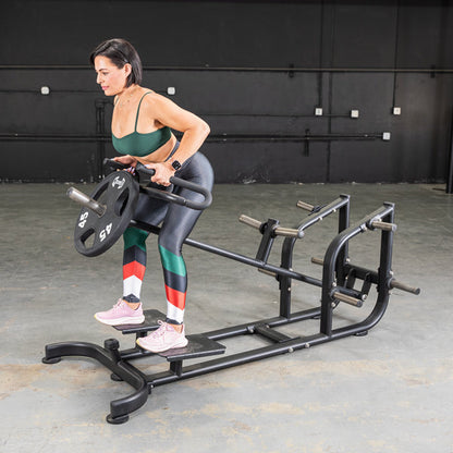 Woman using a T-Bar Row Machine with colorful leggings for strength training.