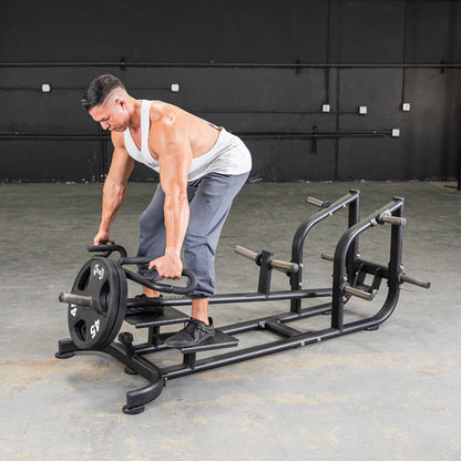Man using T-Bar Row Machine with weighted plates for back workout in gym.