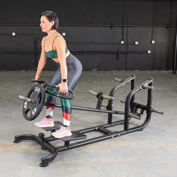 Woman using a black landmine row machine for strength training in a gym.