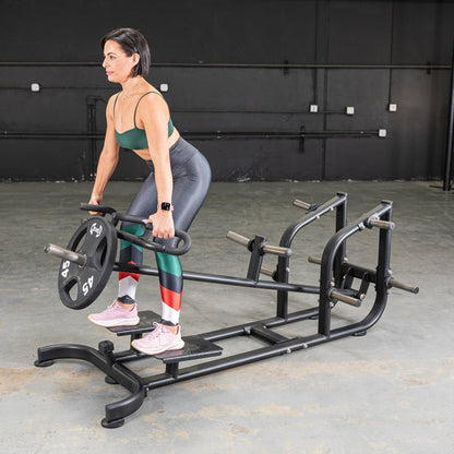 Woman using a black landmine row machine for strength training in a gym.