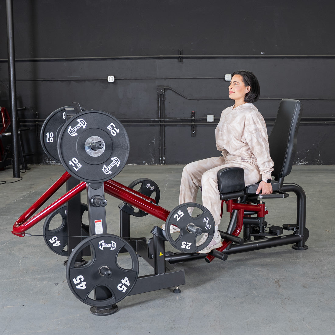 Woman seated at power leverage abductor/adductor machine in gym.