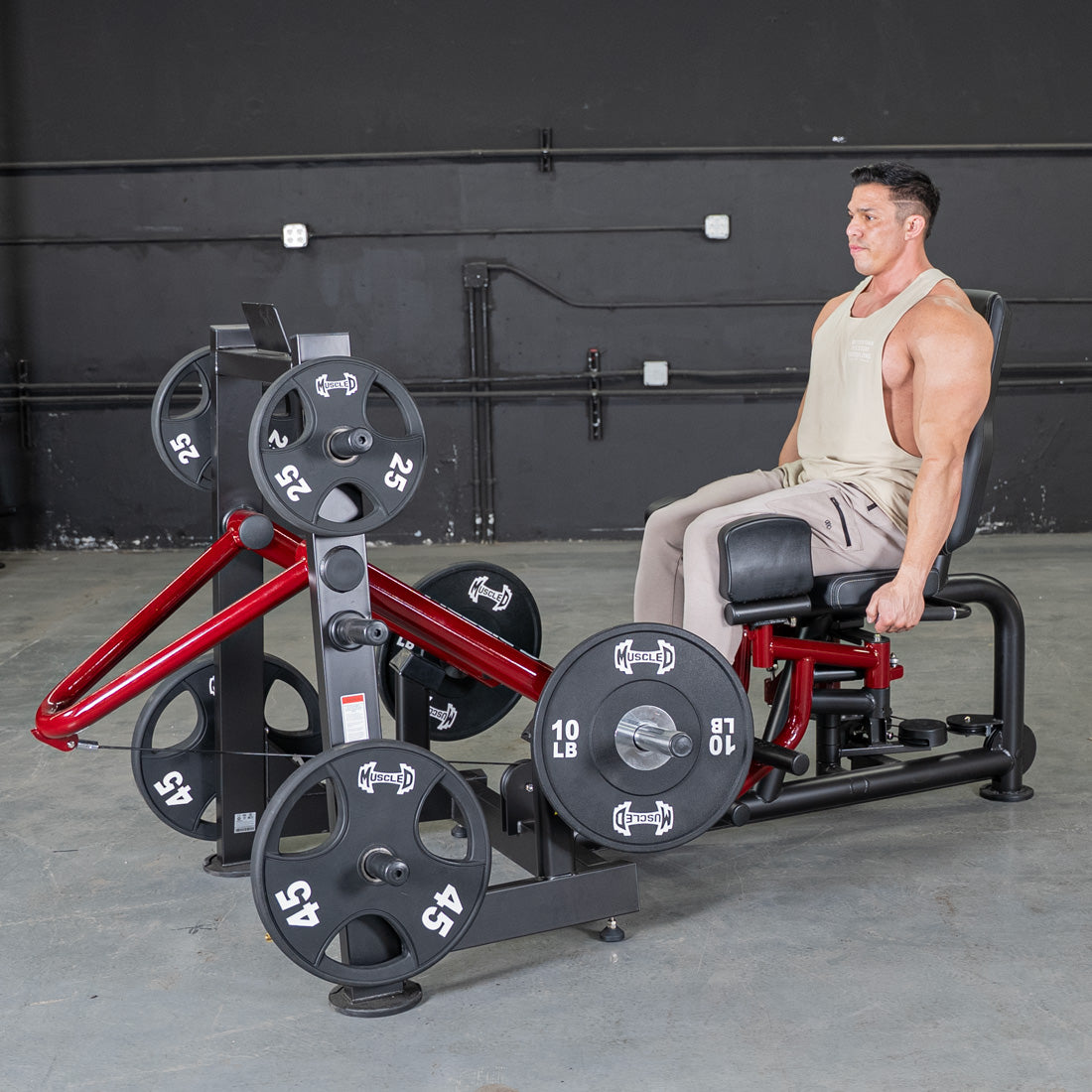 Man seated on leg abductor/adductor machine in gym with weight plates.