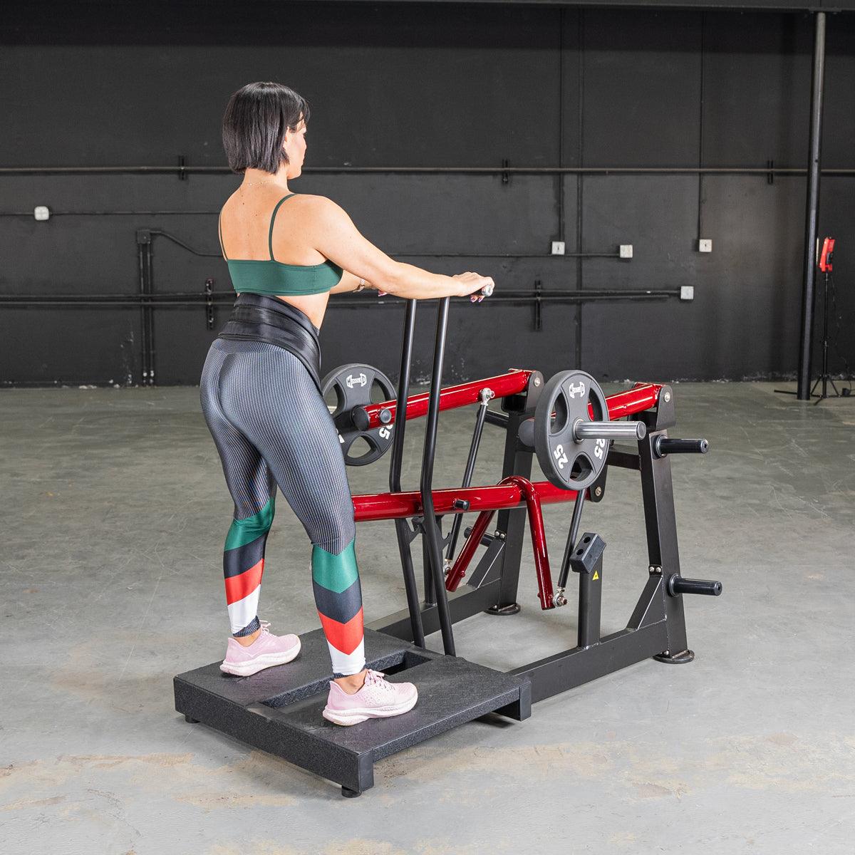 Woman using a belt-squat machine with weight plates in a gym.