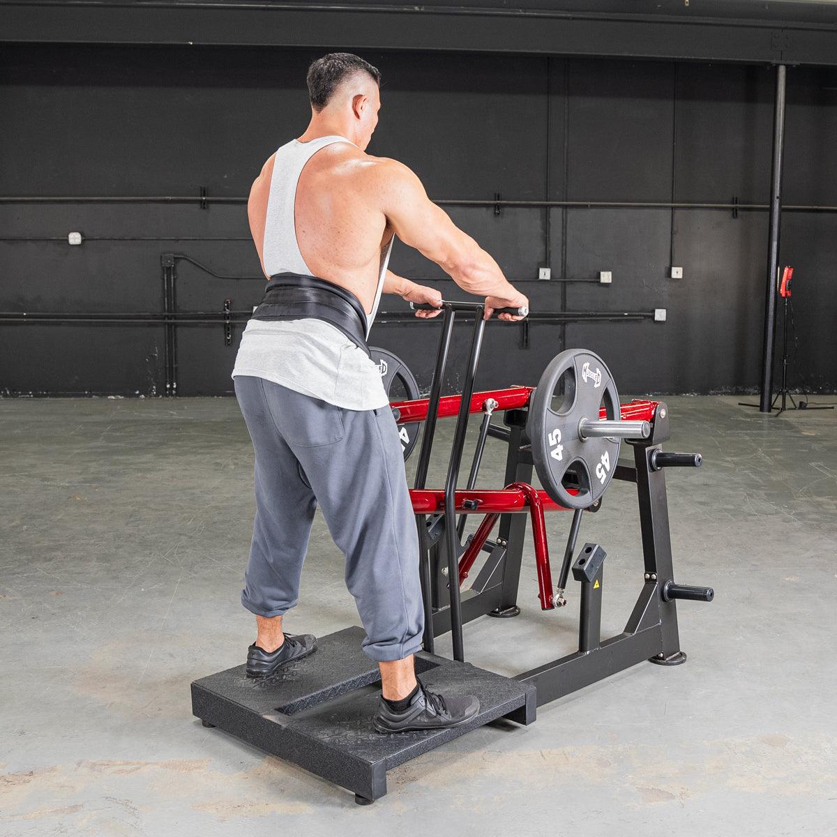 Man using belt squat machine with weights in gym.