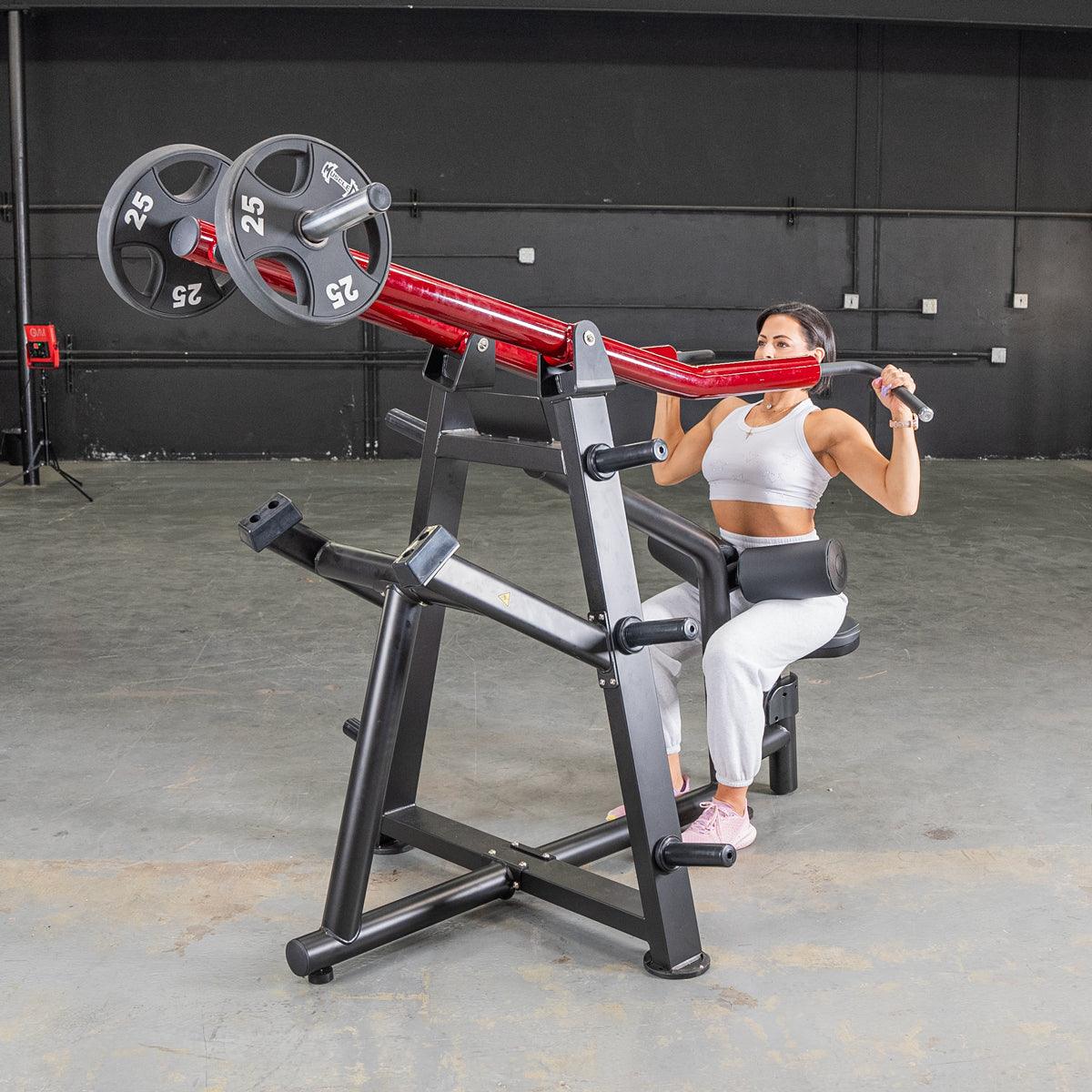 Woman using red and black seated shoulder press machine in gym.