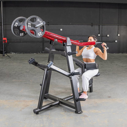 Woman using red and black seated shoulder press machine in gym.