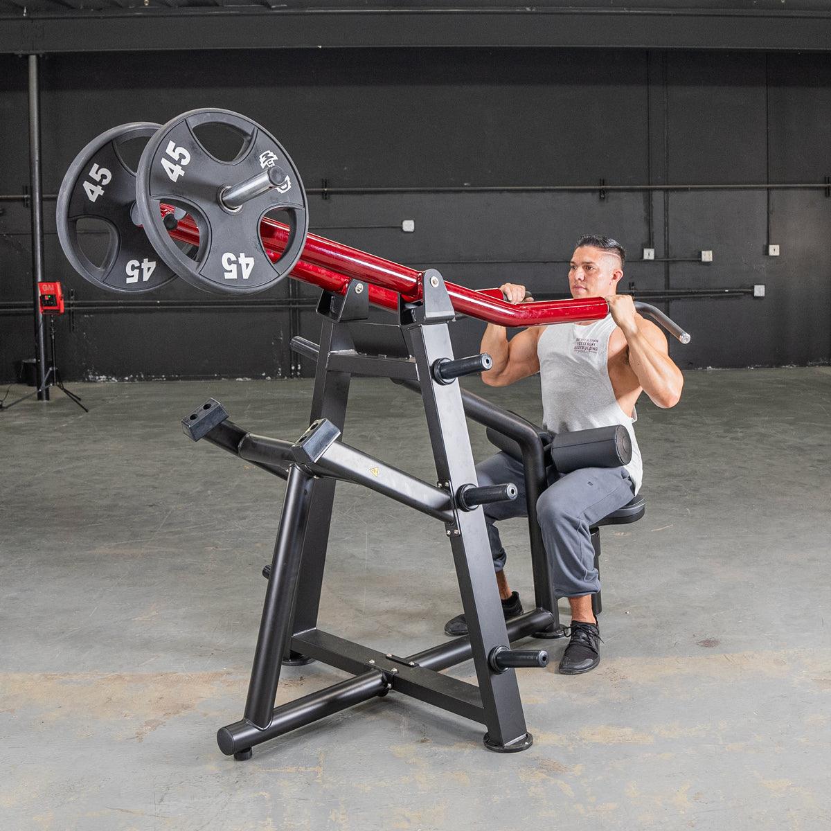 Man using red shoulder press machine with 45 lb weights in gym.