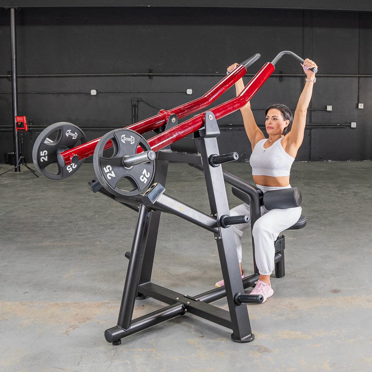 Woman using a red Plate loaded shoulder press machine in a gym.