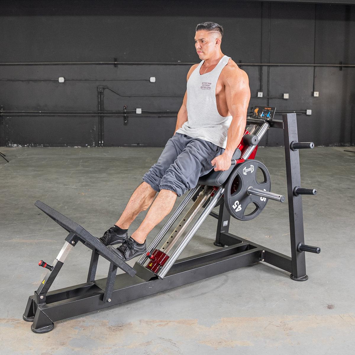 Man seated on power-leverage hack squat machine with calf raise attachment.
