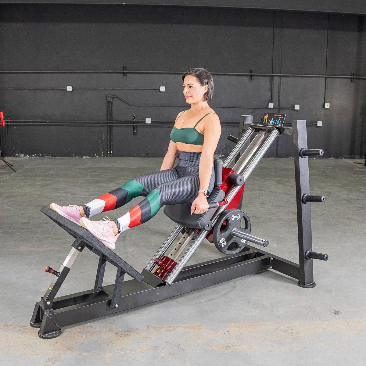 Woman seated on power-leverage hack squat calf-raise machine in a gym.
