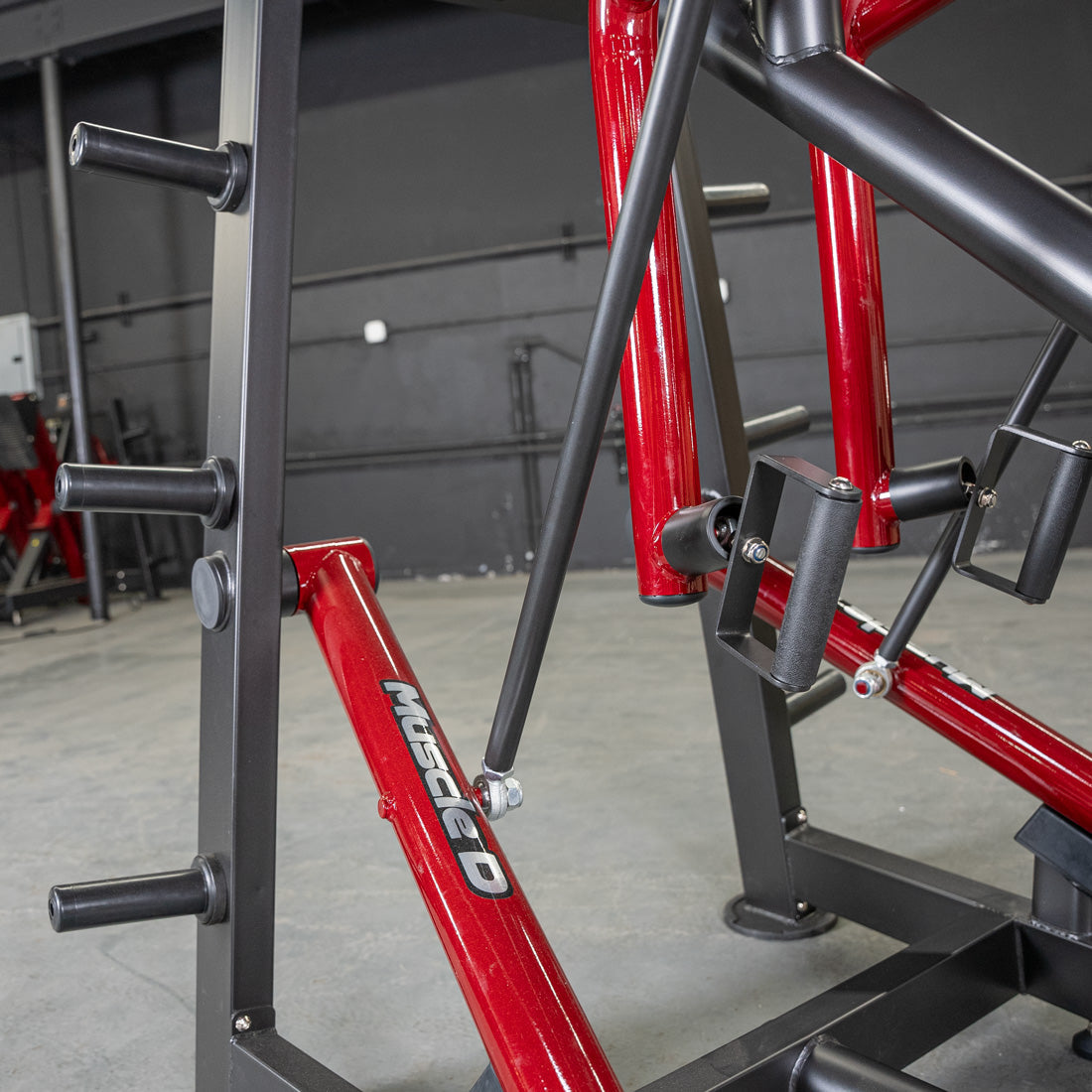 Muscle D red and black gym equipment with weight storage pegs.