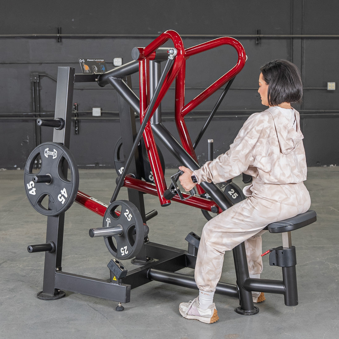 Woman using Body-Solid leverage row machine with red accents in gym.