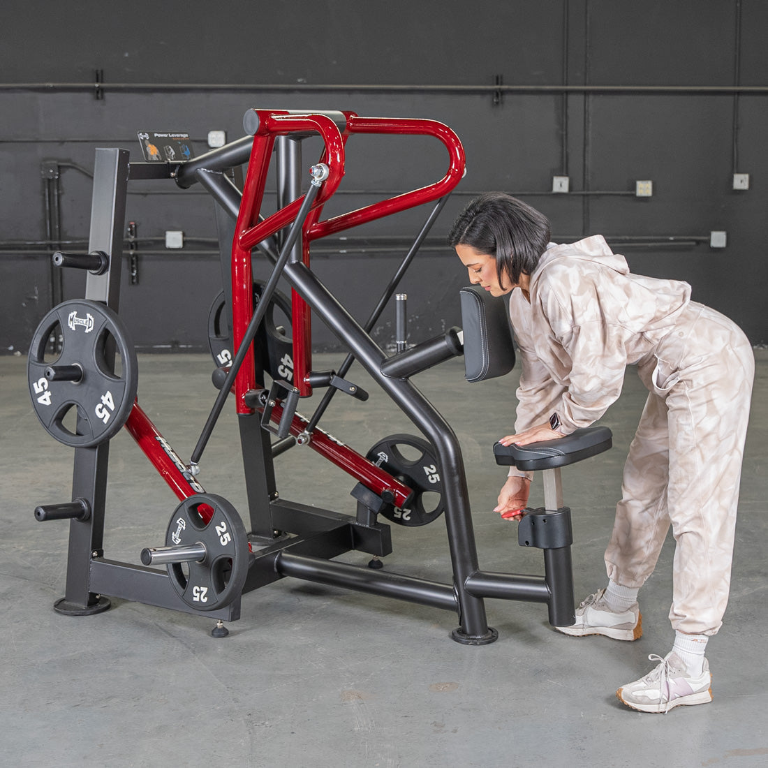 Woman adjusting Power Leverage row machine with red accents in gym.