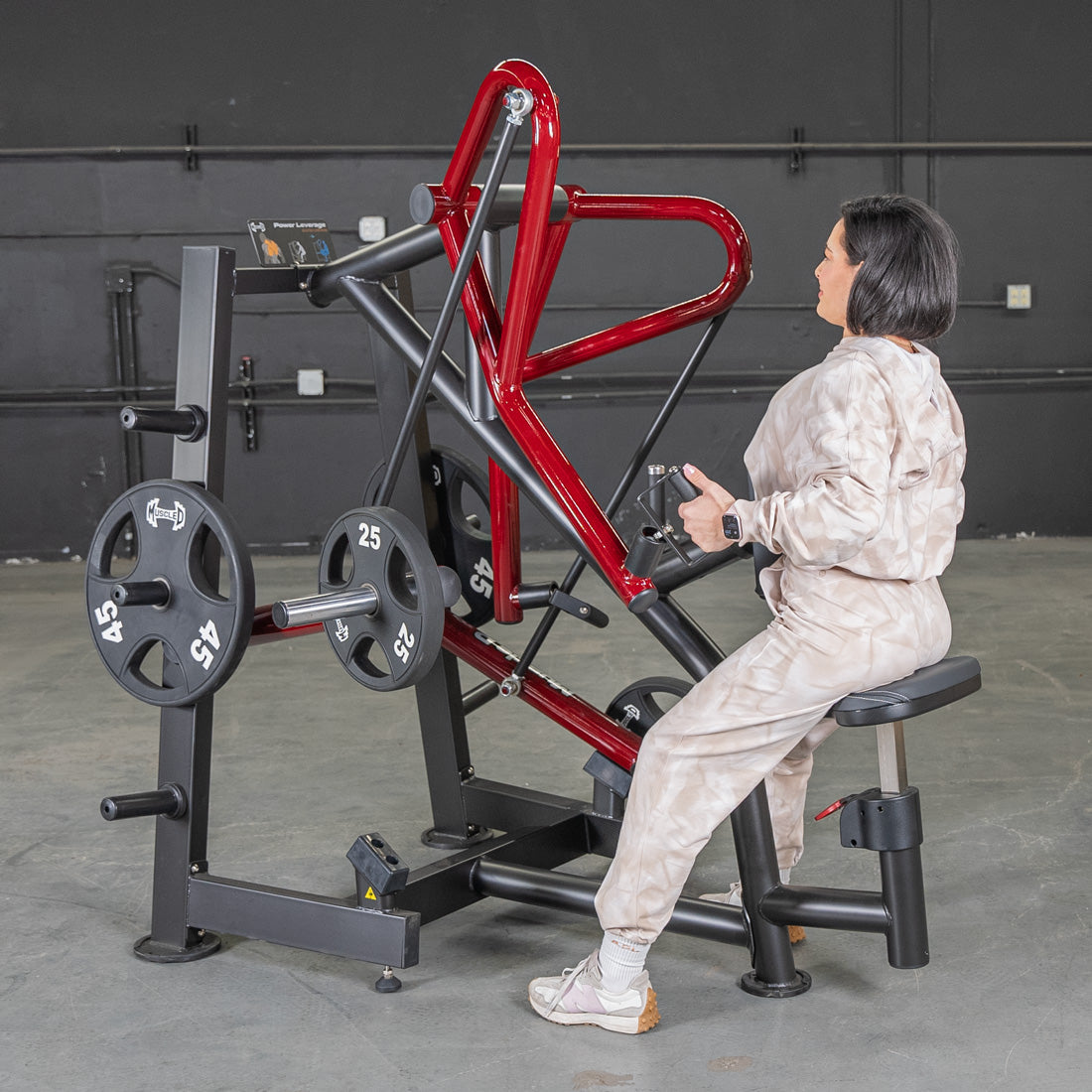 Woman using red and black leverage row machine in gym.