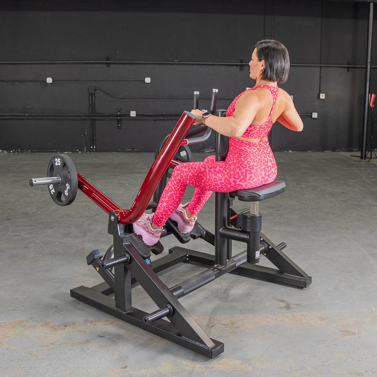 Woman in pink leopard print outfit using a red seated row machine in a gym.