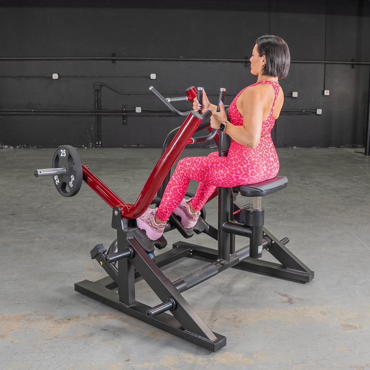 Woman in pink leopard workout set using seated row machine with red frame in gym.