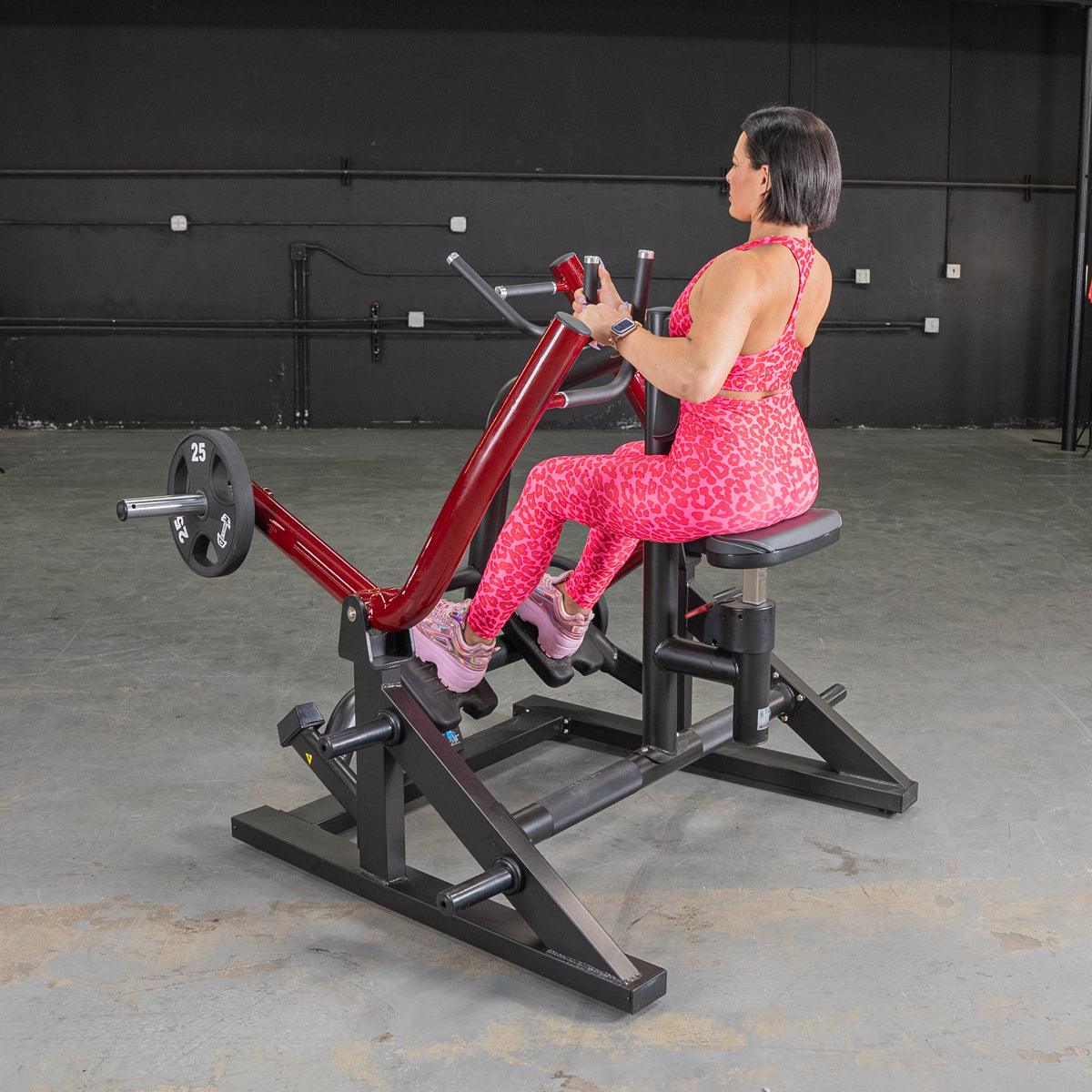 Woman in pink workout attire using a seated row machine with red handles in a gym.