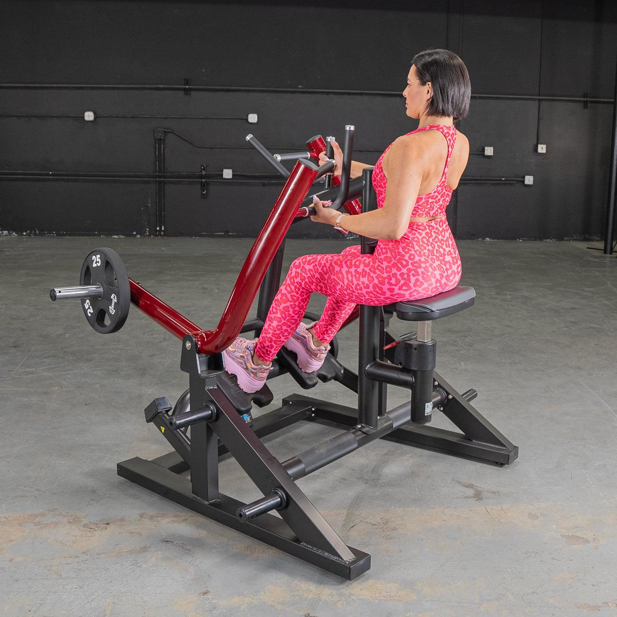 Woman in pink workout outfit using a red seated row machine in a gym.