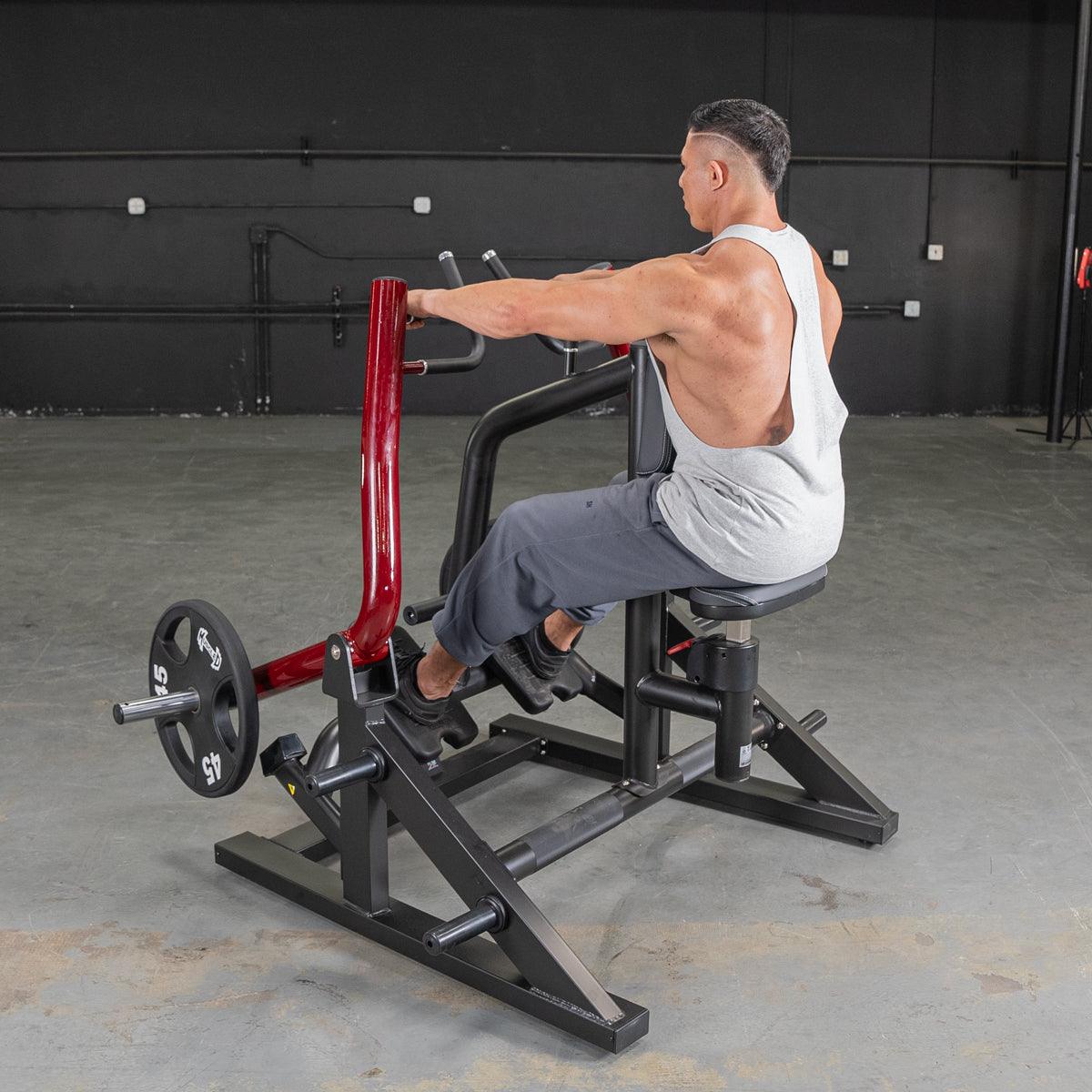 Man using a seated row machine with red handles, wearing a gray tank top in a gym setting.