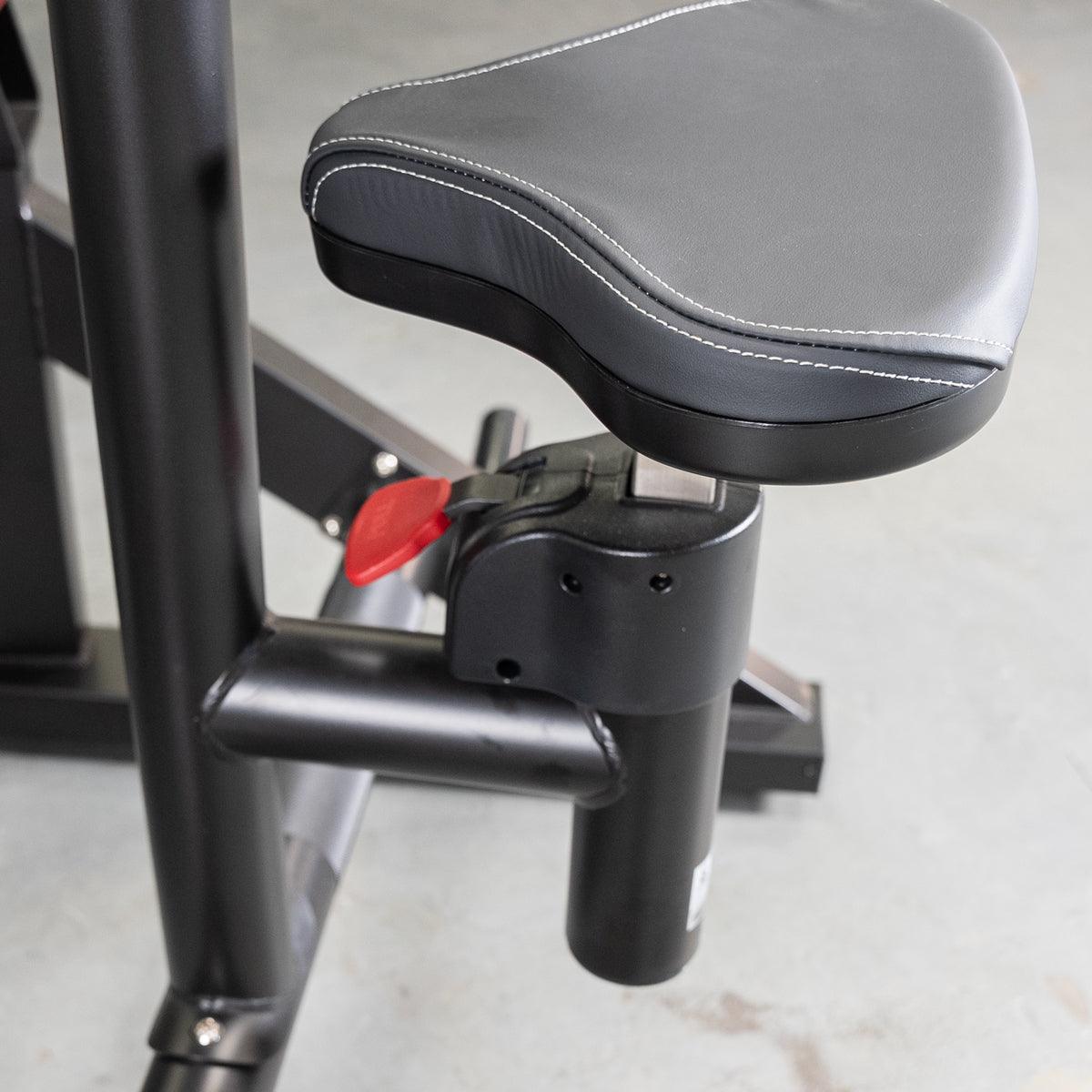 Adjustable gym machine seat with gray leather padding and red lever for height control.